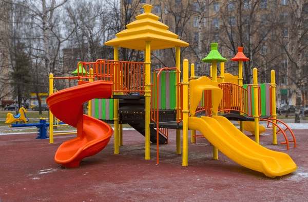 Colourful outdoor school playground with red and yellow slides, climbing platforms, and bright play towers on a safety surface.