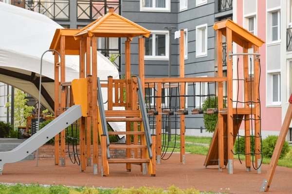 Wooden playground structure with a slide, climbing ropes, and platforms in a residential outdoor play area.