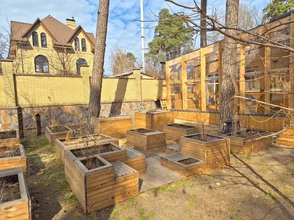 Outdoor garden area with wooden raised planter boxes, decking, trees, and a wooden structure beside a brick wall